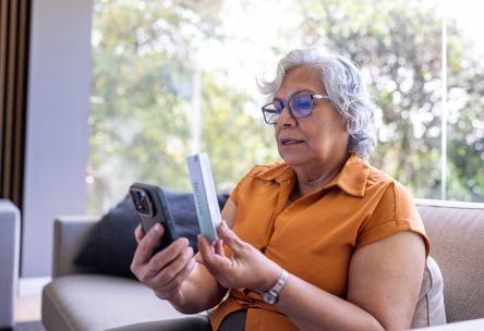 A woman holding a box of medicine to her phone while in a telehealth video call