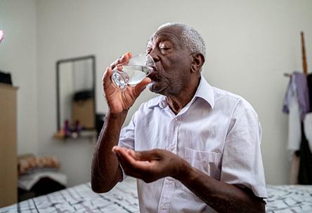 A man holding a pill and drinking from a glass of water